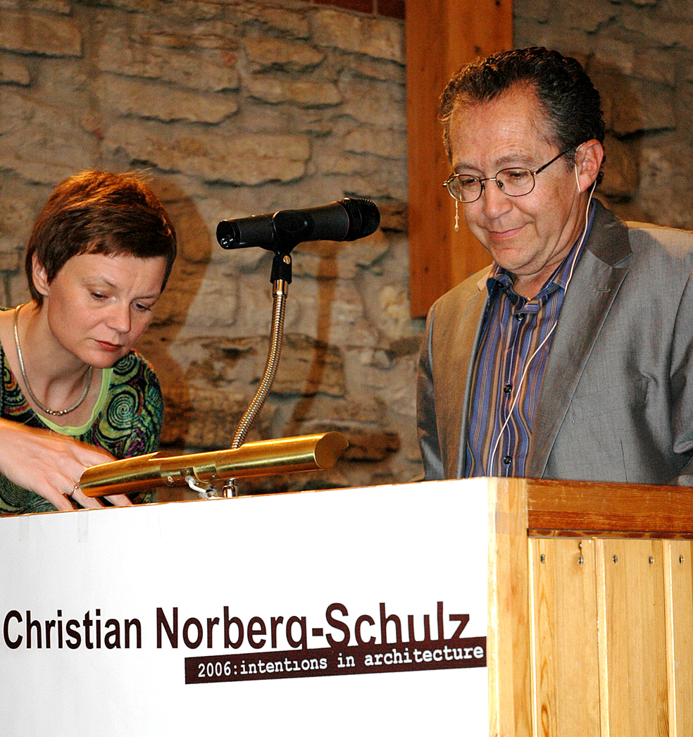 Mari Hvattum rekker en hjelpende hånd til Alberto Pérez-Gómez på talerstolen.