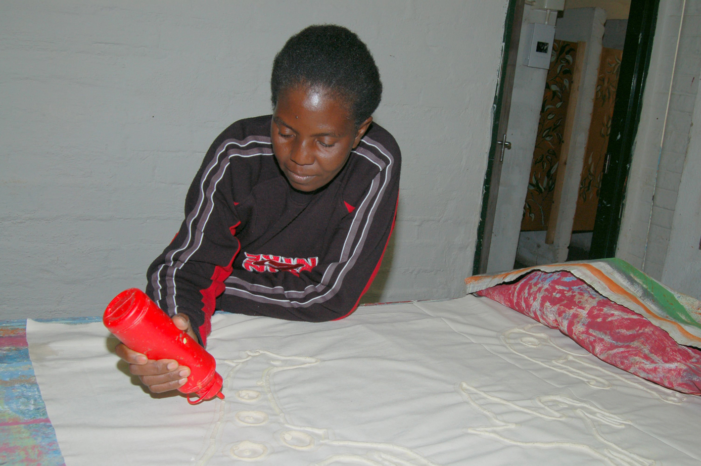 Batikkmønsteret tegnes på stoffet med en blanding av maismel og vann. Loide Mwanyangapo skal lage et veggteppe. Batikkmønsteret tegnes på stoffet med en blanding av maismel og vann. Loide Mwanyangapo skal lage et veggteppe.