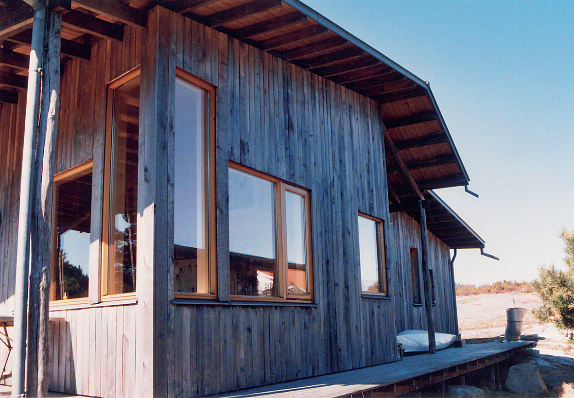 Hytte på Koster tegnet av Arne Henriksen. Bygningen er fem år gammel og har stående 25 mm tykk uhøvlet ospekledning med 5 mm luftespalte. Der er noe skjolder, men synsinntrykket av disse reduseres ved de vertikale brudd i kledningen. Legg merke til at bjelkene under takutstikk er blitt grå.