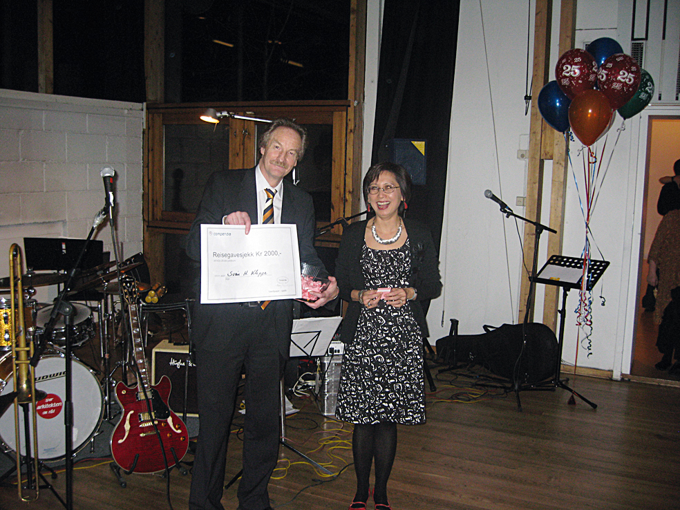 Premieutdelingen etter loddtrekning blant festdeltagerne. Jostein Fyhn overrekker en reisesjekk på kr 2000 fra Compendia til Na Stephansen fra plan- og bygningsetaten i Oslo kommune. Foto: Robert Kjøsnes. Premieutdelingen etter loddtrekning blant festdeltagerne. Jostein Fyhn overrekker en reisesjekk på kr 2000 fra Compendia til Na Stephansen fra plan- og bygningsetaten i Oslo kommune. Foto: Robert Kjøsnes.